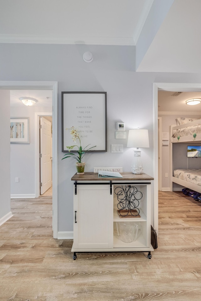 hall featuring visible vents, ornamental molding, light wood-style flooring, and baseboards