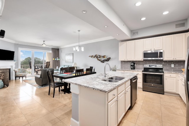 kitchen featuring pendant lighting, ceiling fan with notable chandelier, appliances with stainless steel finishes, a center island with sink, and light stone counters