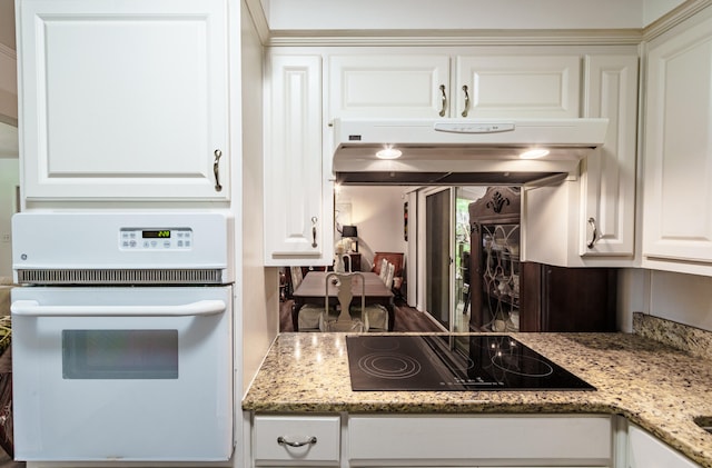 kitchen with black electric cooktop, oven, white cabinetry, and light stone counters