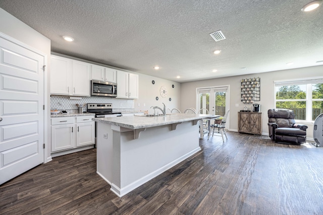 kitchen featuring a kitchen island with sink, white cabinetry, dark wood-type flooring, and stainless steel appliances