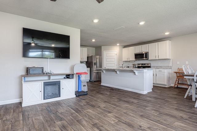 kitchen featuring white cabinetry, an island with sink, dark hardwood / wood-style flooring, stainless steel appliances, and a kitchen bar