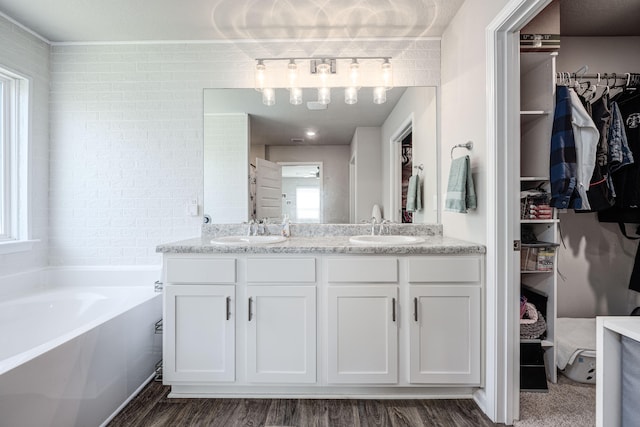 bathroom featuring wood-type flooring, vanity, a bathtub, and brick wall