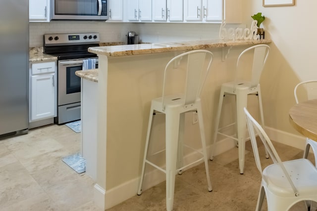 kitchen with light stone countertops, backsplash, stainless steel appliances, white cabinetry, and light tile floors