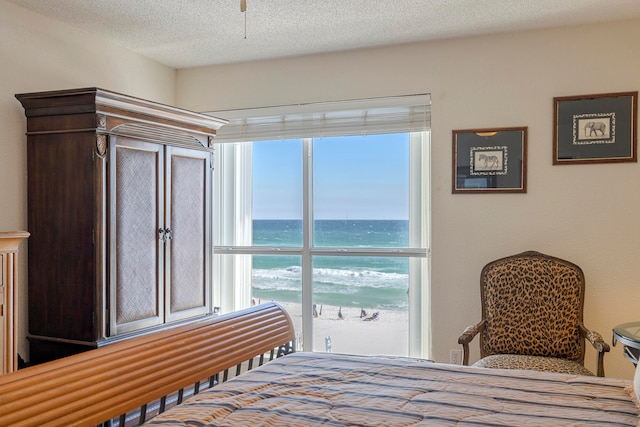 bedroom with a water view, a textured ceiling, and a view of the beach