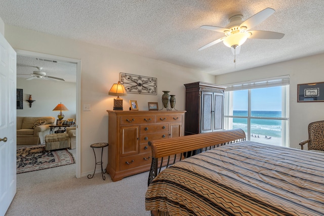 bedroom featuring light carpet, ceiling fan, a textured ceiling, and a water view