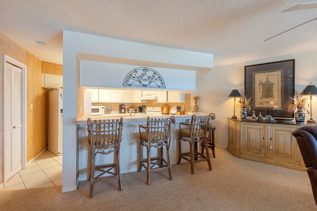 kitchen with a textured ceiling, a kitchen breakfast bar, light carpet, and white appliances