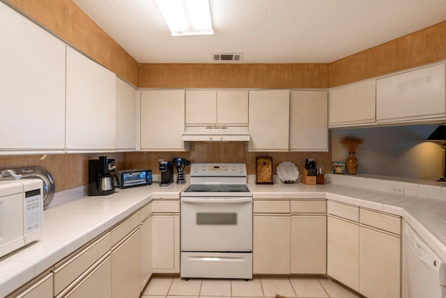 kitchen with white appliances, custom range hood, a textured ceiling, tile countertops, and light tile floors