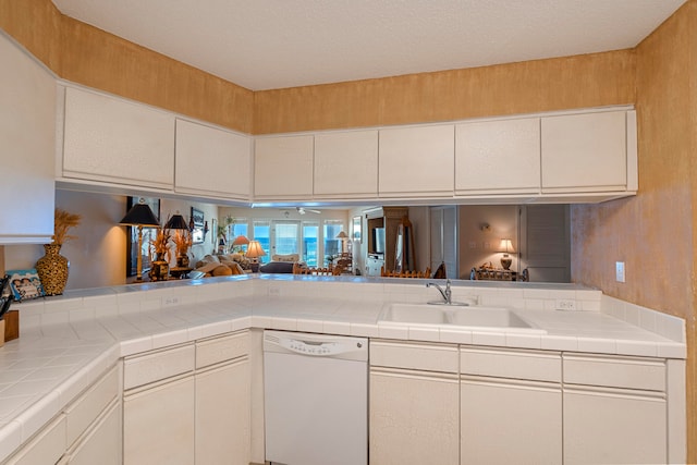 kitchen with tile counters, sink, white dishwasher, and kitchen peninsula