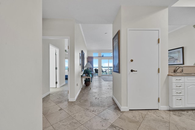 hallway with crown molding, a wall of windows, sink, and light tile flooring