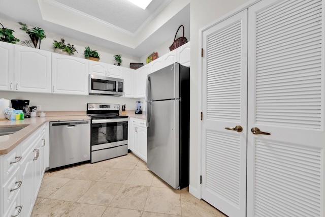 kitchen featuring appliances with stainless steel finishes, light tile floors, a raised ceiling, white cabinetry, and ornamental molding