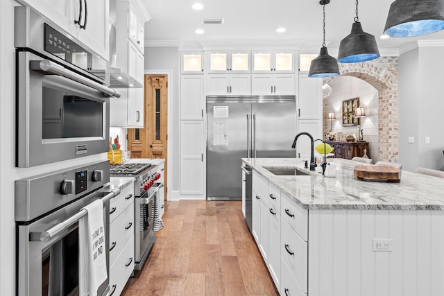 kitchen with high end appliances, pendant lighting, white cabinets, light hardwood / wood-style flooring, and ornamental molding