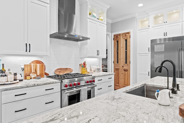 kitchen featuring wall chimney exhaust hood, white cabinets, sink, backsplash, and high end appliances