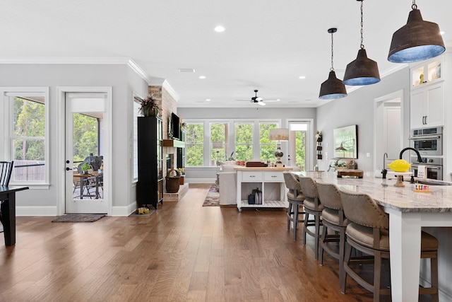 kitchen with a kitchen bar, white cabinets, dark wood-type flooring, hanging light fixtures, and crown molding