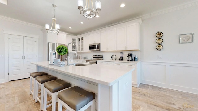 kitchen with decorative light fixtures, stainless steel appliances, an island with sink, white cabinets, and a notable chandelier