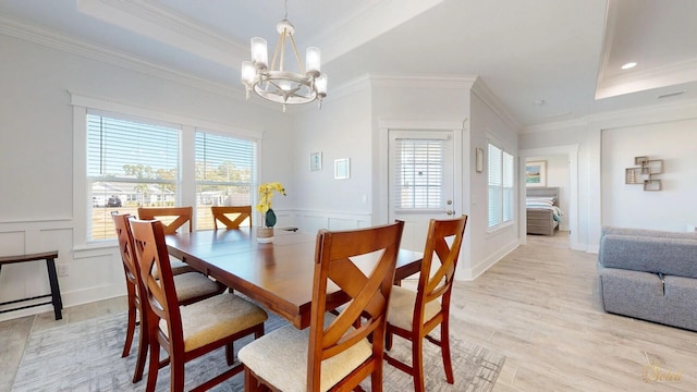 dining space with an inviting chandelier, a healthy amount of sunlight, light hardwood / wood-style floors, and a raised ceiling