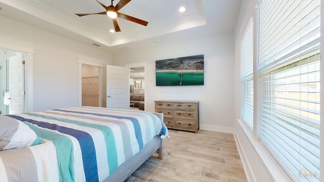 bedroom featuring a closet, light wood-type flooring, a spacious closet, a raised ceiling, and ceiling fan