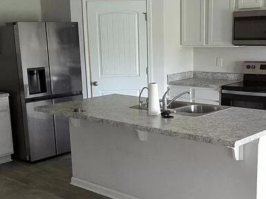 kitchen with white cabinetry, appliances with stainless steel finishes, dark hardwood / wood-style floors, light stone counters, and sink