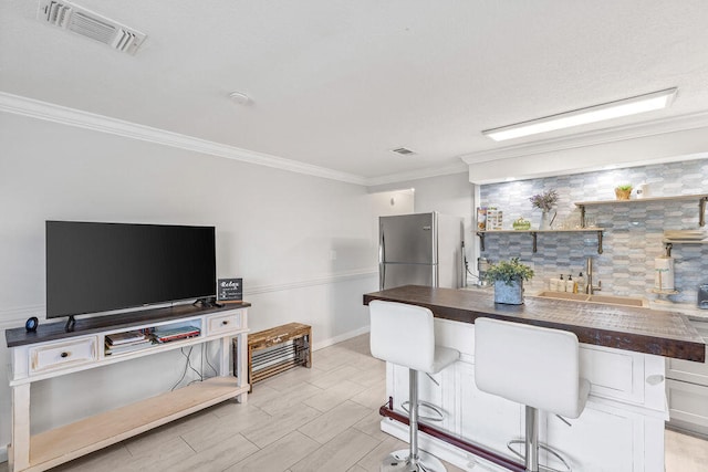 kitchen featuring stainless steel refrigerator, crown molding, backsplash, a kitchen bar, and sink