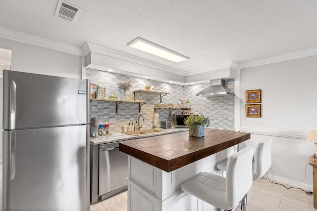 kitchen featuring wall chimney exhaust hood, crown molding, appliances with stainless steel finishes, sink, and tasteful backsplash