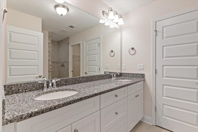 bathroom with tiled shower, a textured ceiling, and vanity