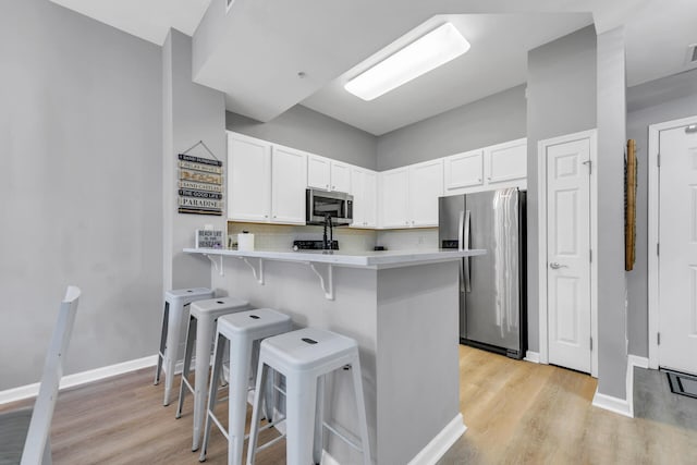 kitchen with stainless steel appliances, white cabinetry, light wood-style floors, light countertops, and a kitchen bar