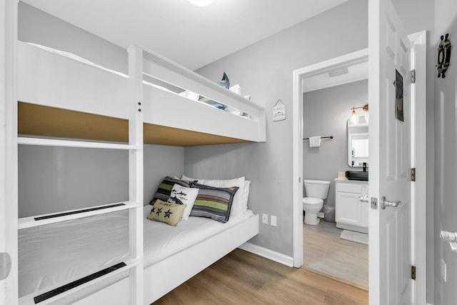 bedroom featuring connected bathroom, baseboards, and wood finished floors