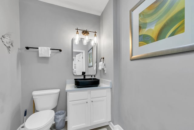 half bathroom featuring toilet, baseboards, and vanity