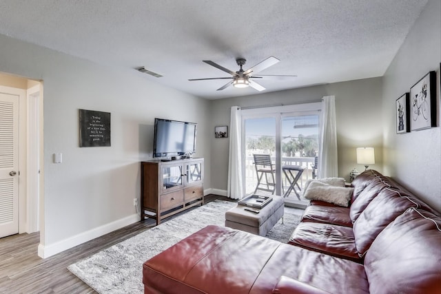 living room featuring a textured ceiling, wood finished floors, visible vents, and baseboards