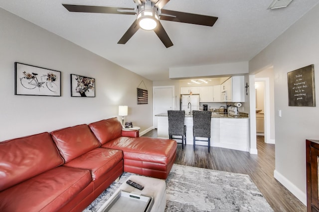 living room featuring dark wood-type flooring, visible vents, baseboards, and a ceiling fan