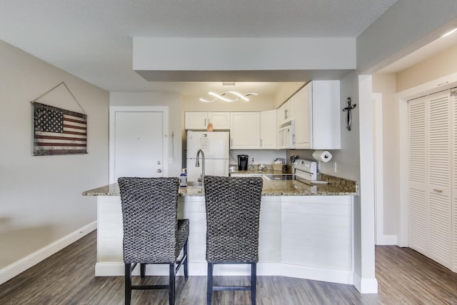 kitchen with a peninsula, white appliances, white cabinets, and light stone countertops