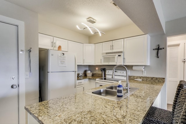 kitchen featuring a textured ceiling, a peninsula, white appliances, and white cabinetry