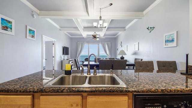 kitchen with coffered ceiling, sink, ceiling fan with notable chandelier, dishwashing machine, and dark stone counters