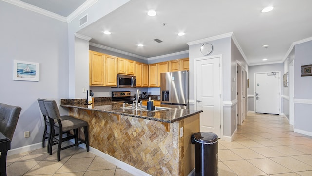 kitchen with appliances with stainless steel finishes, light tile flooring, dark stone counters, crown molding, and a kitchen breakfast bar