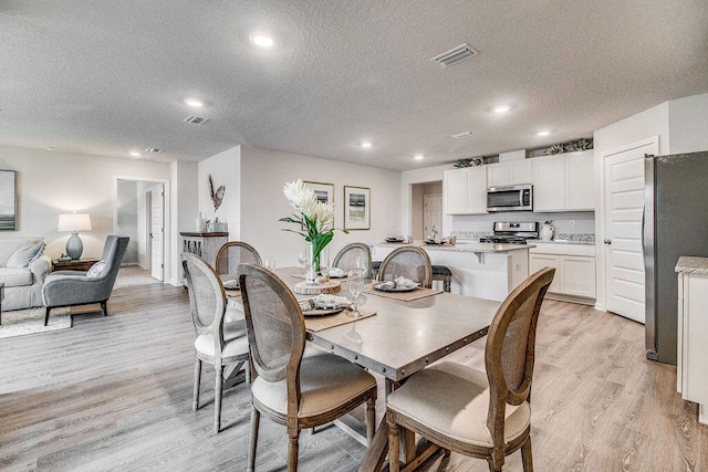 dining space featuring light wood-type flooring and a textured ceiling