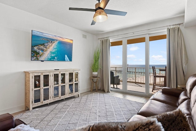 living room with a water view, light hardwood / wood-style flooring, ceiling fan, and a textured ceiling