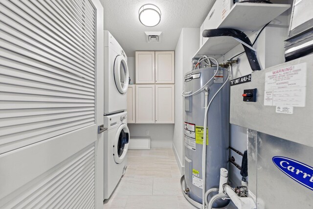 washroom featuring cabinets, stacked washer and dryer, a textured ceiling, water heater, and light tile floors