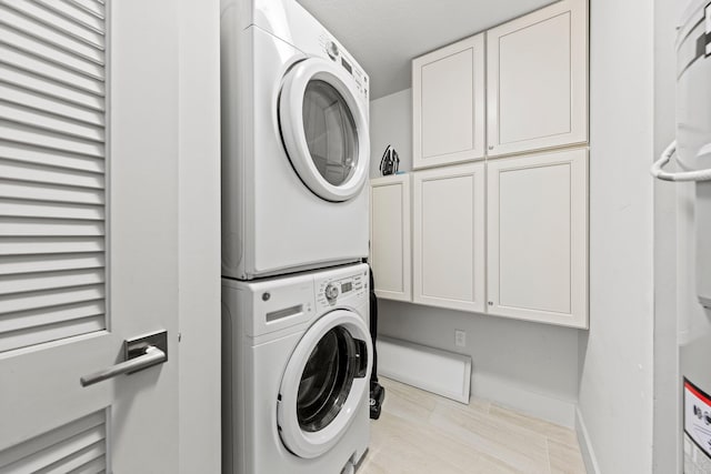 laundry room with cabinets, stacked washer / dryer, and light tile floors