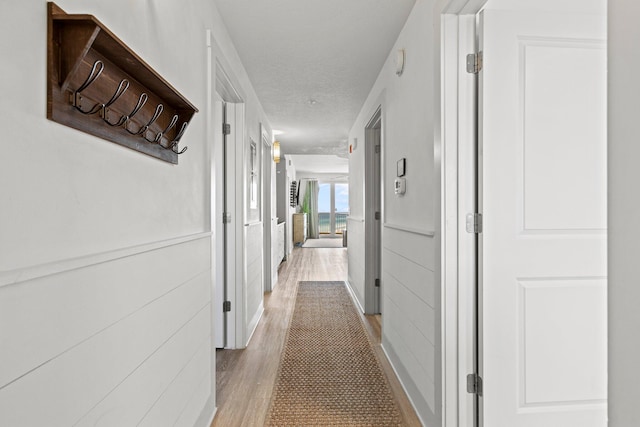 hall with light hardwood / wood-style floors and a textured ceiling