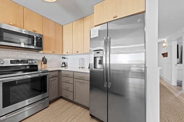 kitchen with backsplash, gray cabinets, stainless steel appliances, light hardwood / wood-style floors, and light brown cabinetry