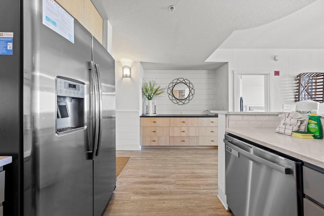 kitchen featuring light wood-type flooring, light brown cabinets, appliances with stainless steel finishes, light stone counters, and a textured ceiling