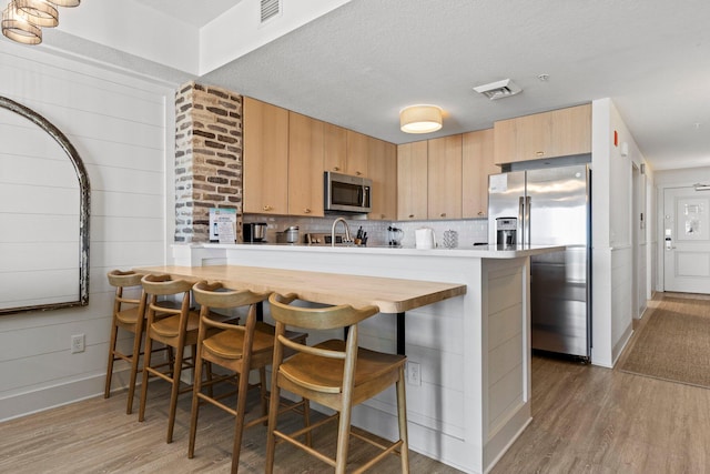 kitchen featuring appliances with stainless steel finishes, a breakfast bar area, backsplash, and light wood-type flooring