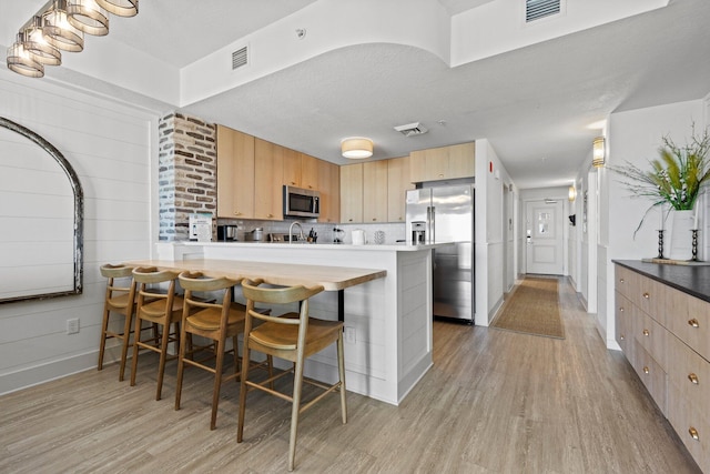 kitchen with light brown cabinetry, light hardwood / wood-style floors, stainless steel appliances, and a breakfast bar