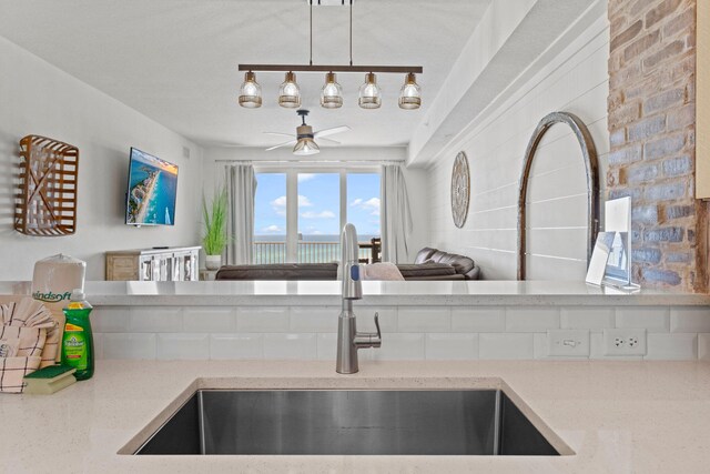 kitchen featuring decorative light fixtures, ceiling fan, light stone counters, rail lighting, and sink