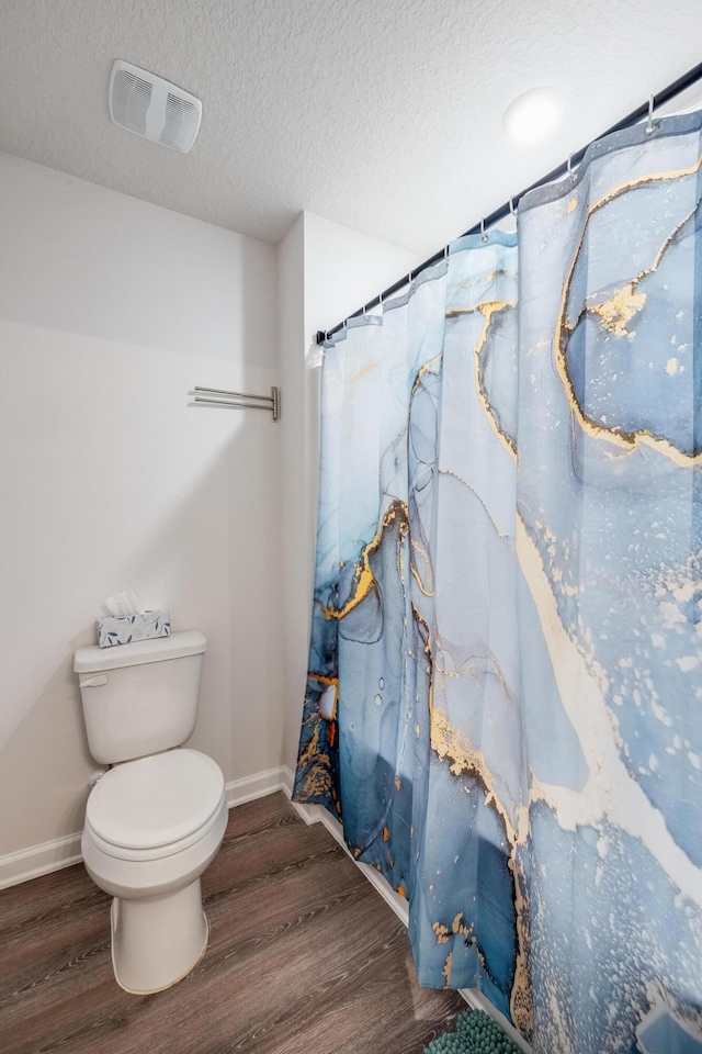 bathroom featuring wood-type flooring, a textured ceiling, toilet, and curtained shower