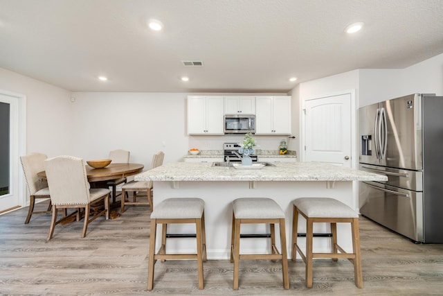 kitchen featuring a center island with sink, light stone countertops, white cabinetry, and stainless steel appliances