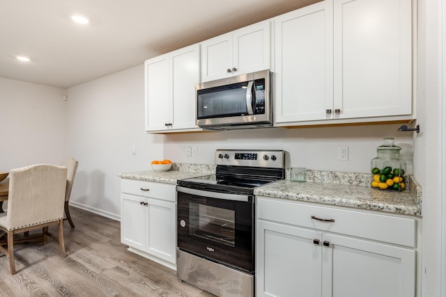 kitchen with white cabinets, light stone counters, light wood-type flooring, and stainless steel appliances