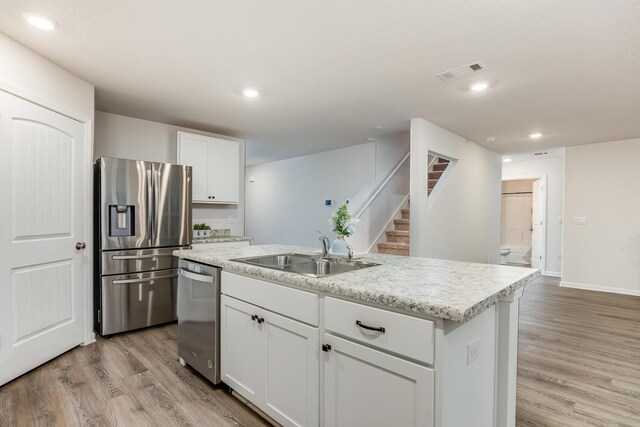 kitchen featuring light wood-type flooring, stainless steel appliances, a kitchen island with sink, sink, and white cabinetry