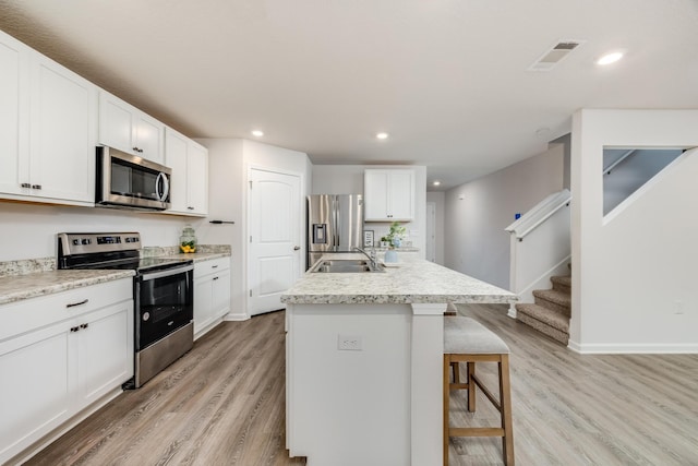 kitchen featuring appliances with stainless steel finishes, light wood-type flooring, a breakfast bar, a kitchen island with sink, and white cabinetry