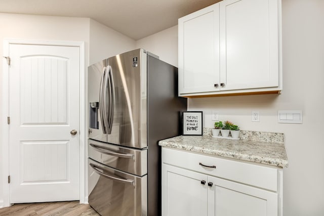 kitchen with stainless steel fridge with ice dispenser, light hardwood / wood-style floors, white cabinetry, and light stone counters