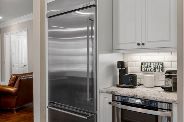 kitchen featuring crown molding, dark hardwood / wood-style flooring, white cabinetry, stainless steel appliances, and tasteful backsplash